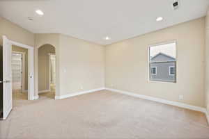Empty room featuring light colored carpet, arched walkways, and recessed lighting
