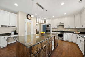 Dual tone kitchen with dark stone counters, arched walkways, a kitchen island, stainless steel appliances, and dark wood-type flooring