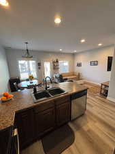 Kitchen featuring light wood-type flooring, dark wood finish cabinetry, dishwasher, pendant lighting, and open floor plan