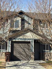 View of side of property with concrete driveway, stone siding, and an attached garage