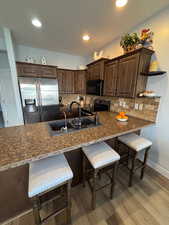 Kitchen featuring dark wood finish cabinets, a kitchen breakfast bar, stainless steel appliances, light wood-style flooring, and a peninsula