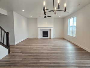 Unfurnished living room featuring wood finished floors, a ceiling fan, hanging lights, and a fireplace