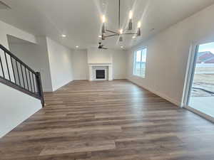 Unfurnished living room featuring a chandelier, ceiling fan, a fireplace, and wood finished floors