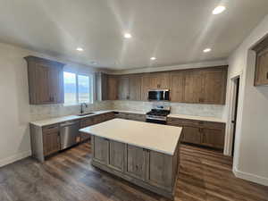 Kitchen with stainless steel appliances, backsplash, a kitchen island, dark wood-style floors, and recessed lighting