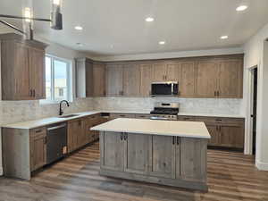 Kitchen with stainless steel appliances, a kitchen island, backsplash, dark wood-type flooring, and wood finish cabinets
