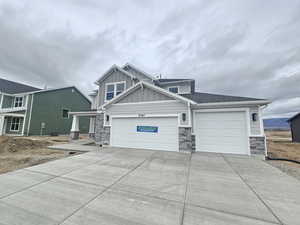 Craftsman-style house with driveway, an attached garage, stone siding, and board and batten siding