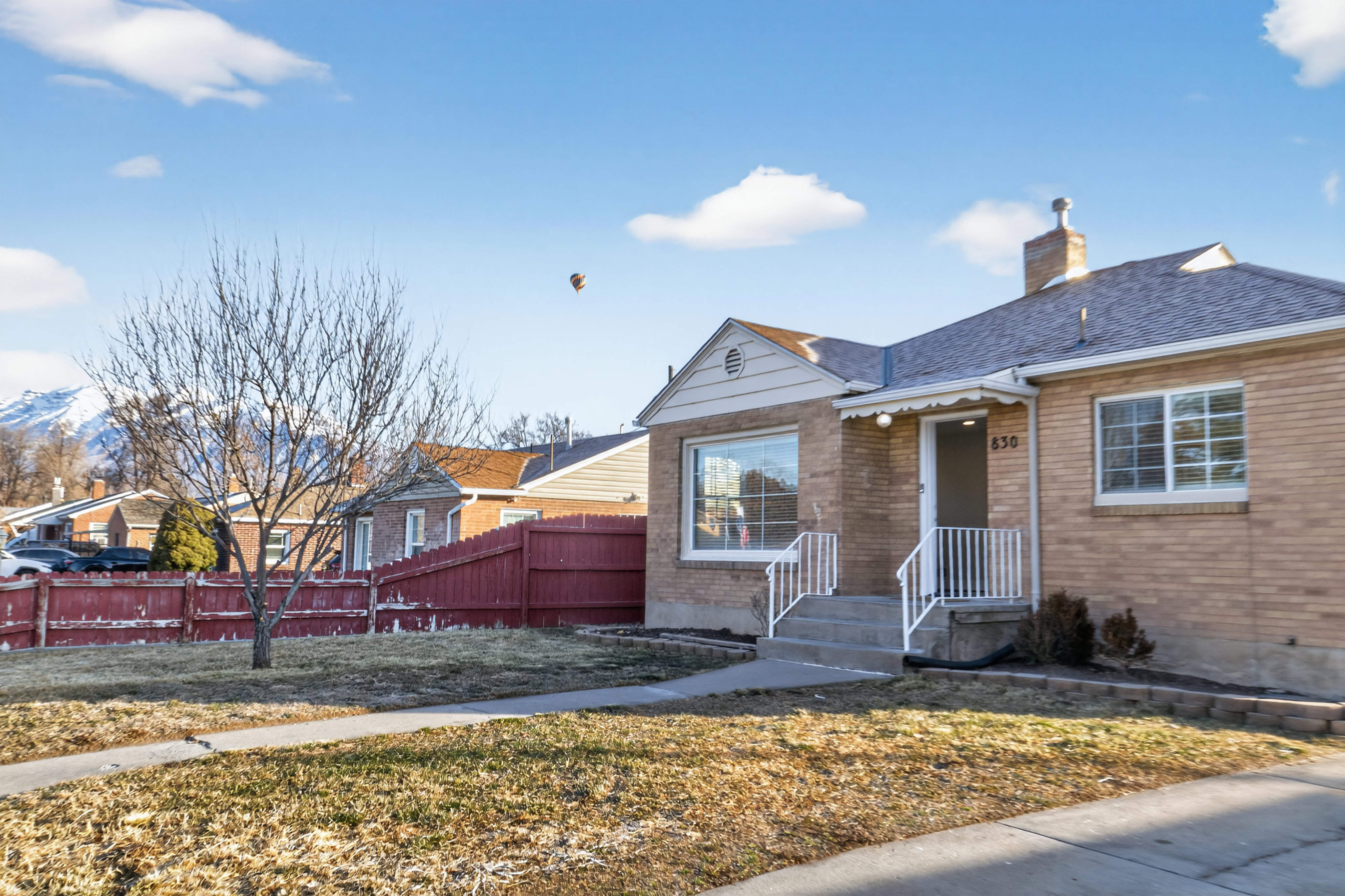 View of front of property featuring a chimney, a shingled roof, and brick siding. Do you see what is in the sky?