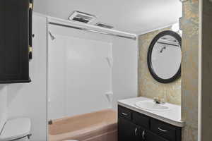 Bathroom with wallpapered walls, vanity, and shower / bath combination