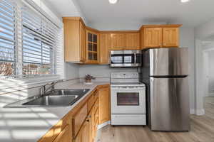 Kitchen with stainless steel appliances, light wood-style flooring, glass insert cabinets, and wood finish cabinetry