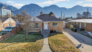 Bungalow-style home featuring brick siding, a chimney, a mountain view, a shingled roof, and concrete driveway