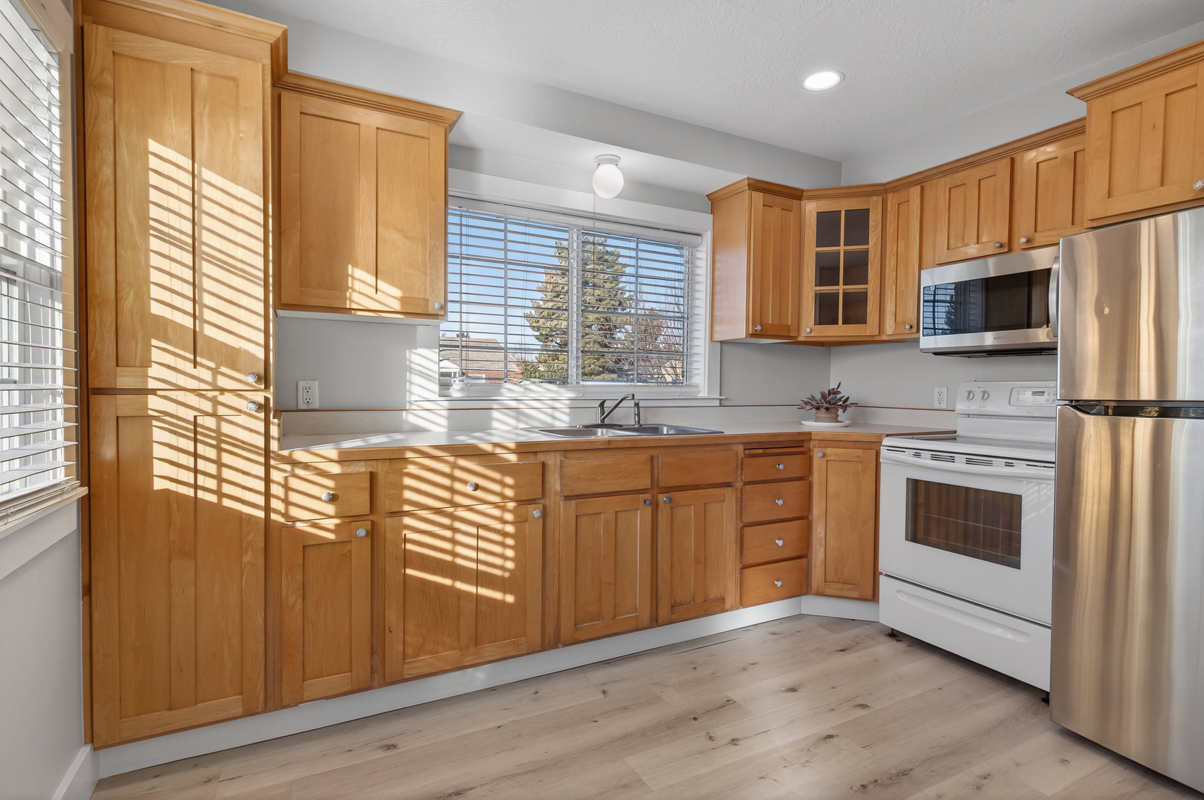 Kitchen with stainless steel appliances, light countertops, light wood-style floors, glass fronted cabinets, and recessed lighting