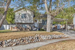Tri-level home featuring a carport, driveway, brick siding, and a storage unit