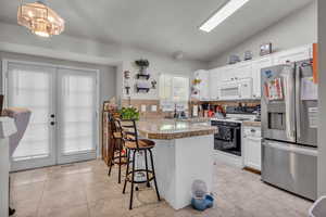 Kitchen featuring stainless steel refrigerator with ice dispenser, range with electric cooktop, a kitchen breakfast bar, vaulted ceiling, and white cabinetry
