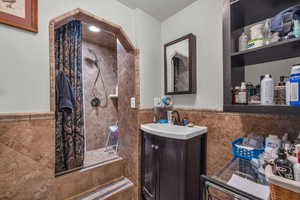 Full bathroom with tile walls, a wainscoted wall, a stall shower, and vanity