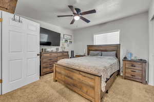 Bedroom featuring a ceiling fan, light carpet, and a textured ceiling