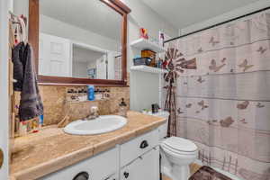 Bathroom featuring a shower with shower curtain, vanity, and backsplash
