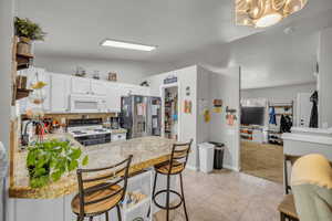 Kitchen featuring a breakfast bar area, white cabinetry, a peninsula, range with electric stovetop, and stainless steel refrigerator with ice dispenser