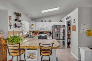 Kitchen with stainless steel refrigerator with ice dispenser, vaulted ceiling, a breakfast bar, electric stove, and a peninsula