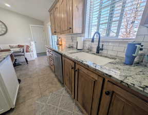 Kitchen featuring lofted ceiling, light stone counters, stainless steel dishwasher, tasteful backsplash, and wood finish cabinets
