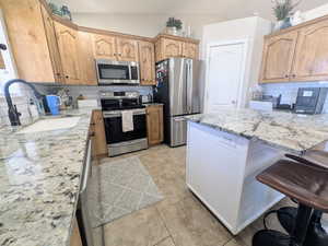 Kitchen featuring light stone countertops, decorative backsplash, a breakfast bar, stainless steel appliances, and lofted ceiling