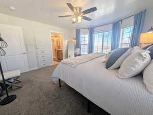 Carpeted bedroom with ensuite bath, a textured ceiling, and a ceiling fan