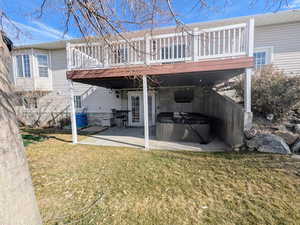 Back of house featuring a hot tub, a patio, a lawn, and a wooden deck
