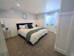 Carpeted bedroom featuring a decorative wall, wainscoting, and recessed lighting
