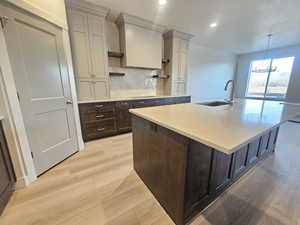 Two tone kitchen featuring two tone color scheme, open shelves, light wood-type flooring, a center island with sink, and light stone countertops