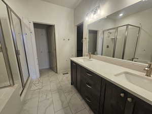 Bathroom featuring a stall shower, double vanity, and light marble finish floors