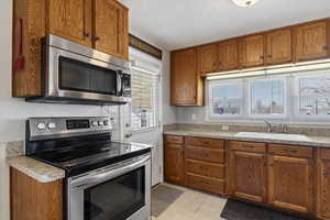Kitchen with stainless steel appliances, wood finish cabinetry, light countertops, light tile patterned floors, and a textured ceiling
