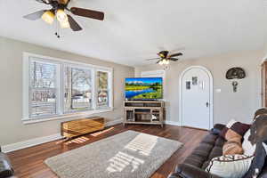 Living room with a ceiling fan, dark wood-type flooring, arched walkways, and a textured ceiling