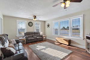Living room featuring a ceiling fan, dark wood-style flooring, and a textured ceiling