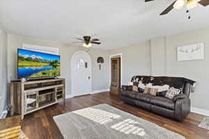 Living room featuring ceiling fan, a textured ceiling, dark wood-style flooring, and arched walkways