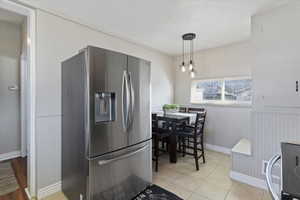 Kitchen with stainless steel refrigerator with ice dispenser, a wainscoted wall, electric stove, and hanging light fixtures