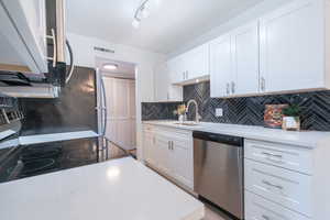 Kitchen featuring stainless steel appliances, white cabinets, light stone countertops, and decorative backsplash