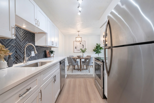 Kitchen featuring stainless steel appliances, white cabinets, light wood-style flooring, and light stone countertops