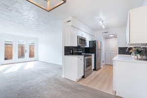 Kitchen with white cabinetry, decorative backsplash, stainless steel appliances, light colored carpet, and french doors
