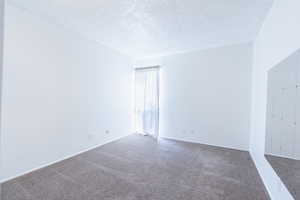 Carpeted empty room featuring a textured ceiling and baseboards