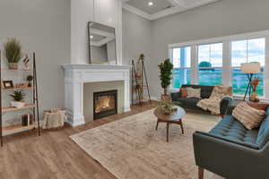 Living area featuring light wood-style floors, ornamental molding, recessed lighting, high coffered ceiling, and a glass covered fireplace