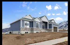 View of front of house featuring a mountain view, stone siding, an attached garage, and a shingled roof
