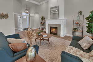 Living area featuring a high ceiling, wood finished floors, a chandelier, ornamental molding, and a glass covered fireplace