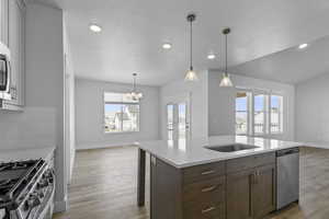 Kitchen featuring open floor plan, light wood finished floors, a kitchen island with sink, and a textured ceiling