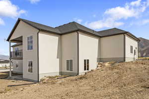 View of property exterior featuring a mountain view, a patio area, a balcony, a shingled roof, and stucco siding
