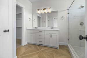 Bathroom with double vanity, a tile shower, and a walk in closet