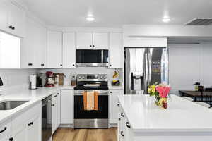 Basement Kitchen with stainless steel appliances, white cabinets, light stone countertops, light wood finished floors, and a center island