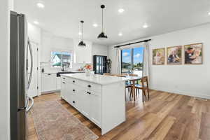 Kitchen with freestanding refrigerator, light wood-style flooring, hanging light fixtures, and white cabinetry