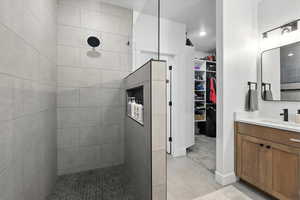 Primary Bathroom featuring tiled shower, vanity, a spacious closet, and light tile patterned flooring