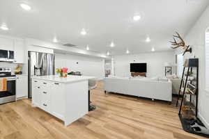 Basement Kitchen with white cabinetry, a breakfast bar, stainless steel appliances, light wood-style flooring, and recessed lighting