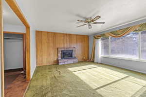 Unfurnished living room featuring wood walls, a ceiling fan, a fireplace, and a textured ceiling
