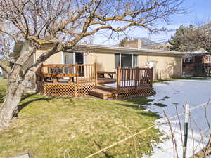 Rear view of house featuring brick siding, a chimney, a lawn, and a deck